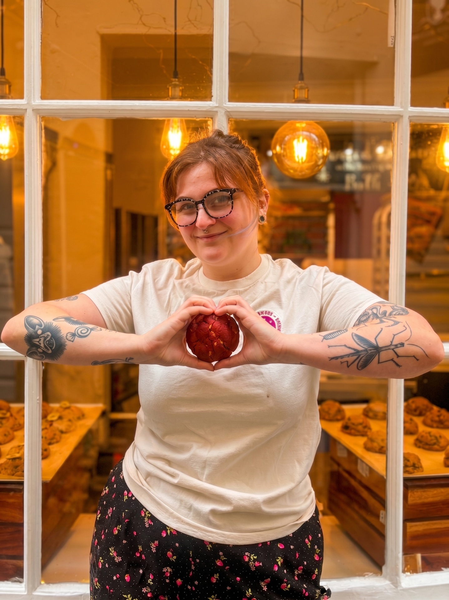 A Bakervee baker holding a red velvet cookie in a heart shape outside the Bath shopfront